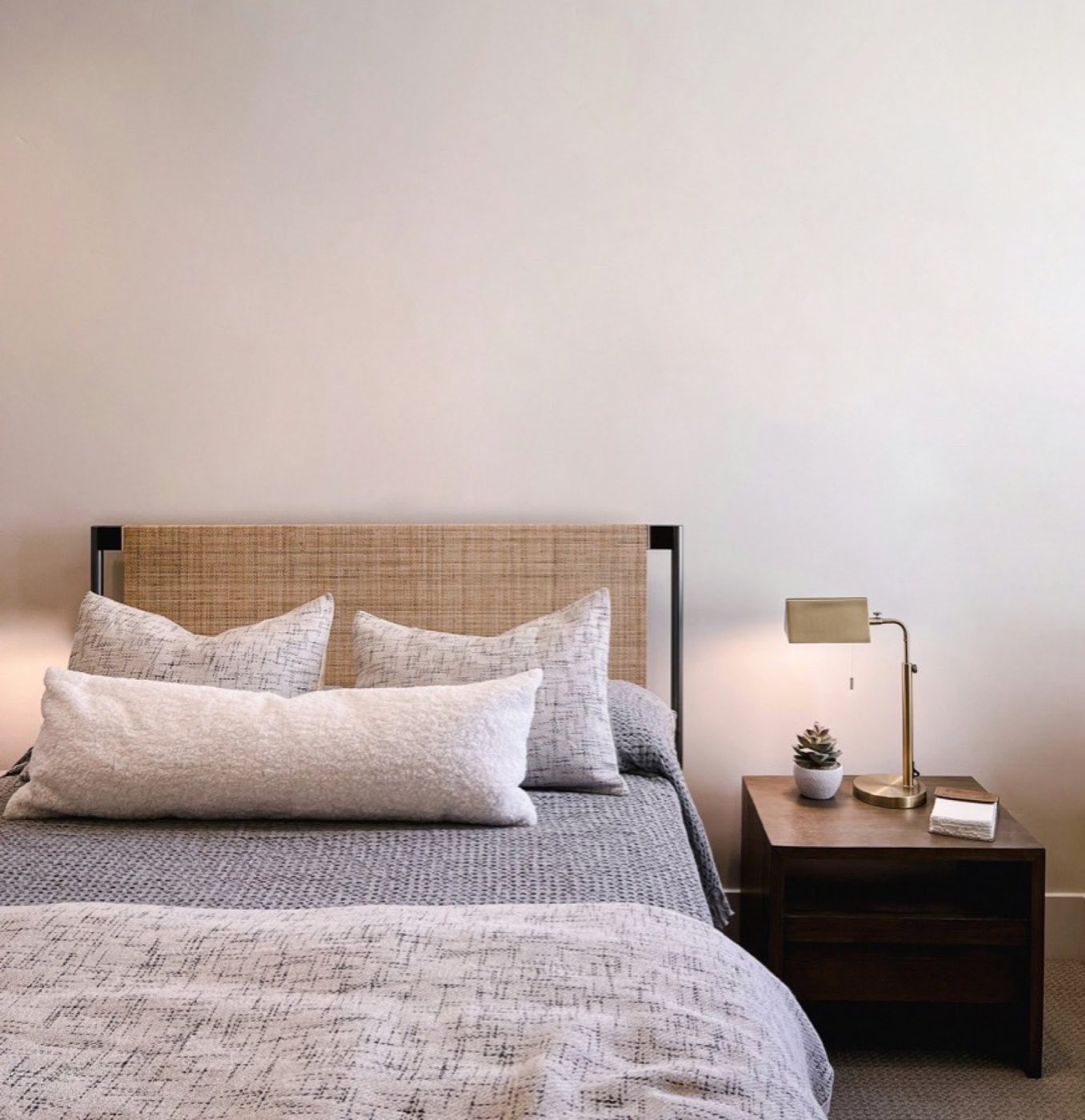 A calm, simply furnished bedroom with a made bed and a bedside lamp